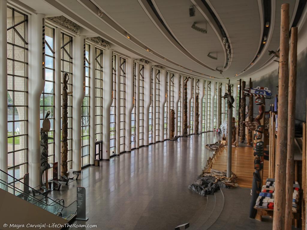 A light-filled gallery with a tall, curved glass enclosure and totem poles
