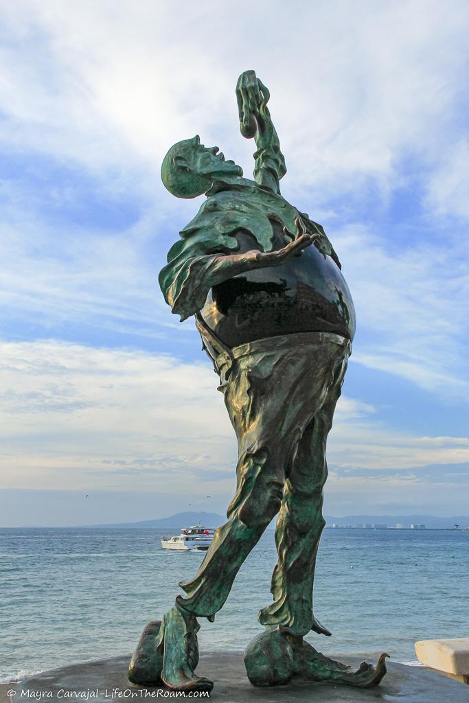 A bronze sculpture of an anthropomorphic figure with the sea as a background