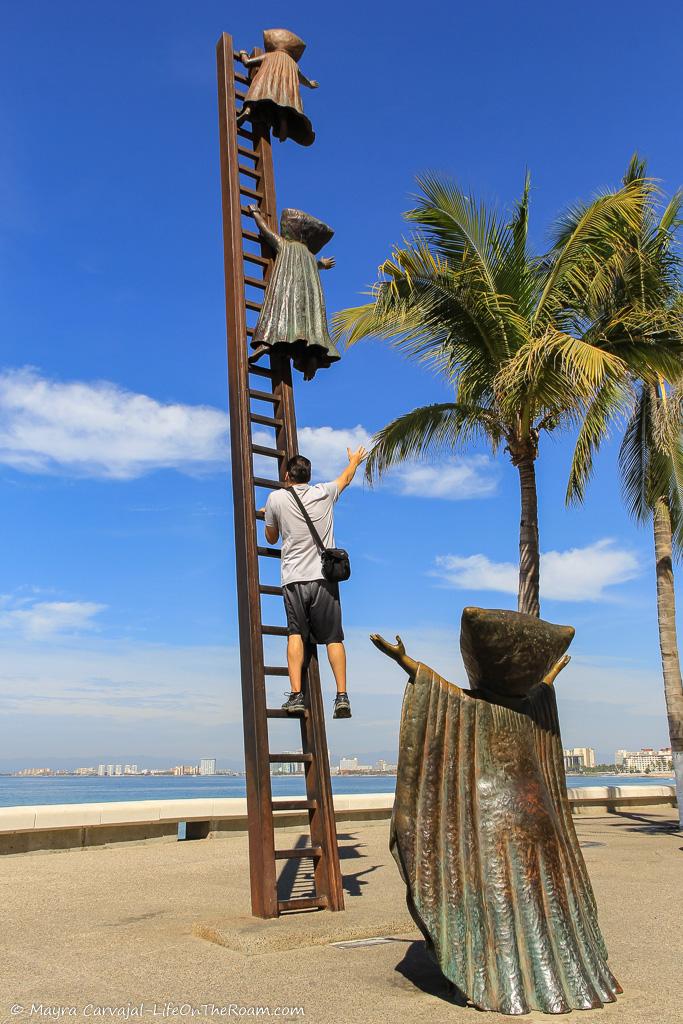 A bronze sculpture of two figures resembling kids going up a ladder, with the sea in the background