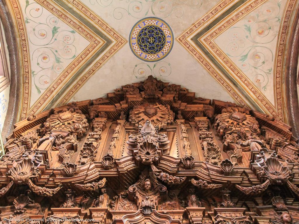 A zoom of wood carvings in an altar and a decorated ceiling in a church