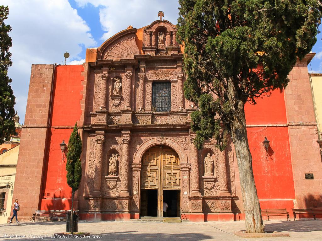 A church with a pink stone façade and a flat, broken shell at the top