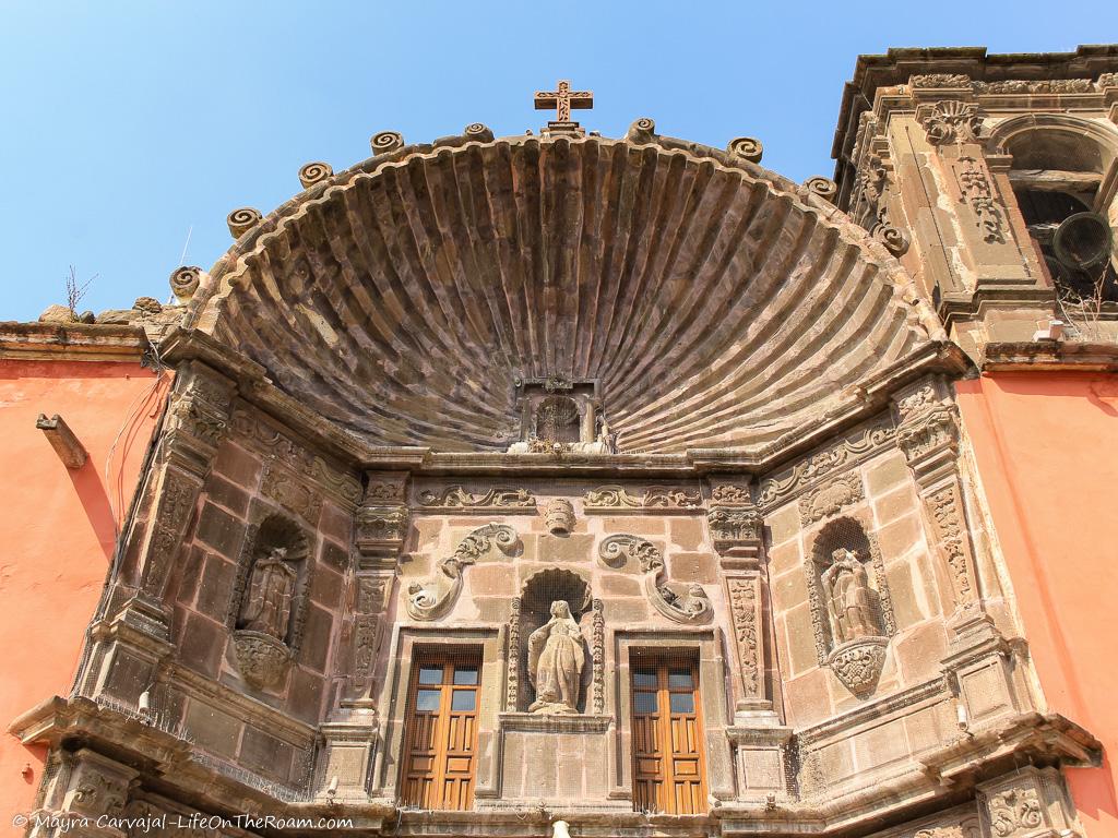 A zoom of the upper part of the façade of a church with a carved shell on top and niches below