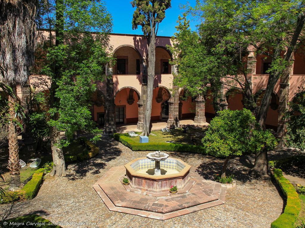 A sunny inner patio with a fountain and tall trees