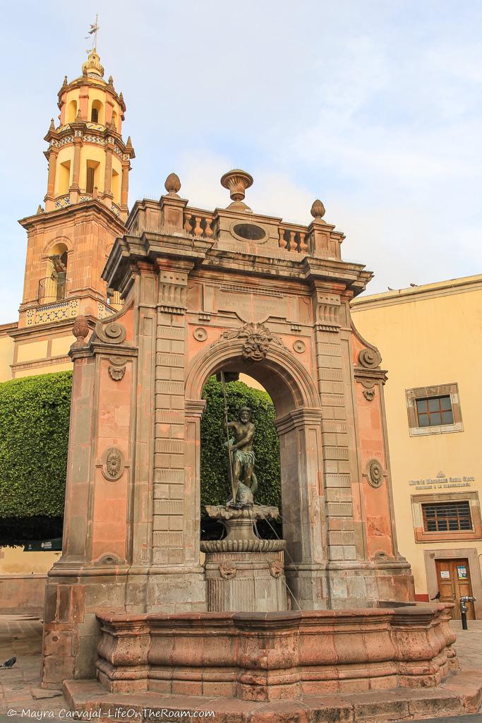 A monumental fountain with a church tower in the background