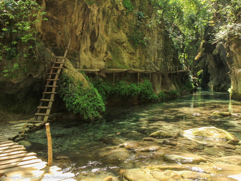 A wood ladder to a bridge anchored to a river canyon wall