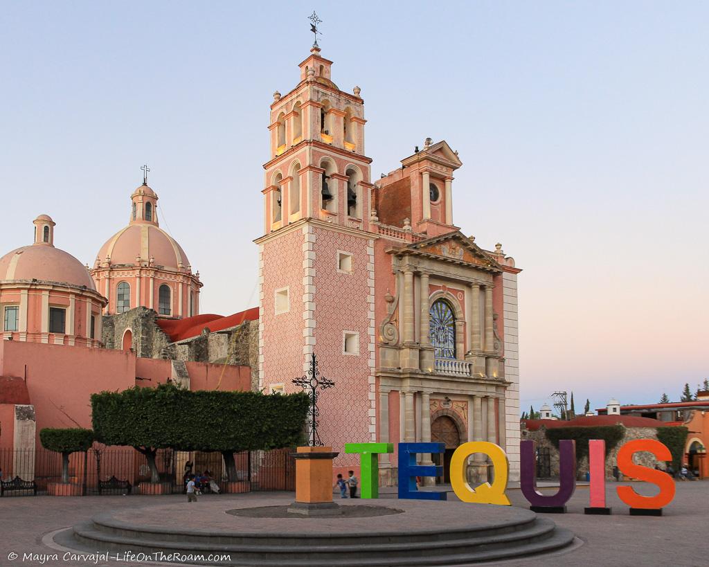 A pink church in a colonial town with the letter TEQUIS