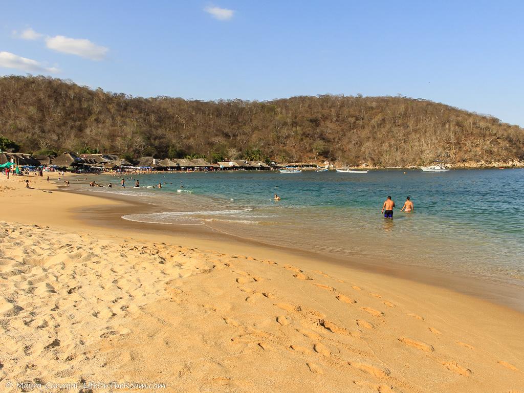 A sandy beach with restaurants and mountains in the background