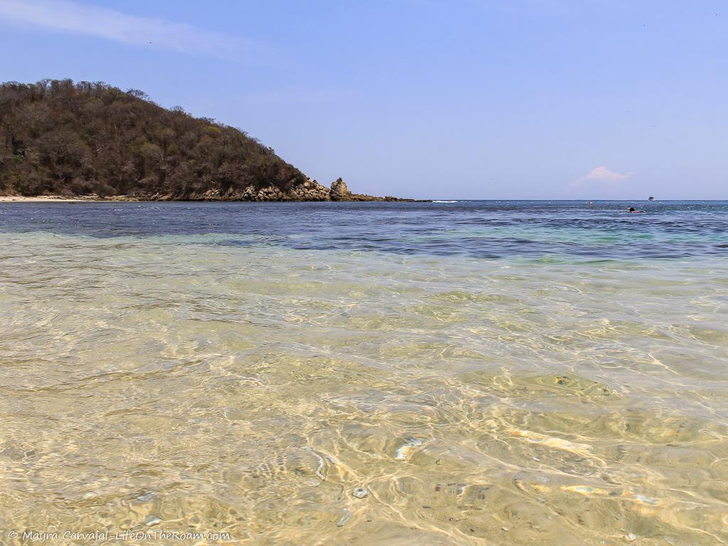 A crystal-clear water beach with some coral and a hill in the background