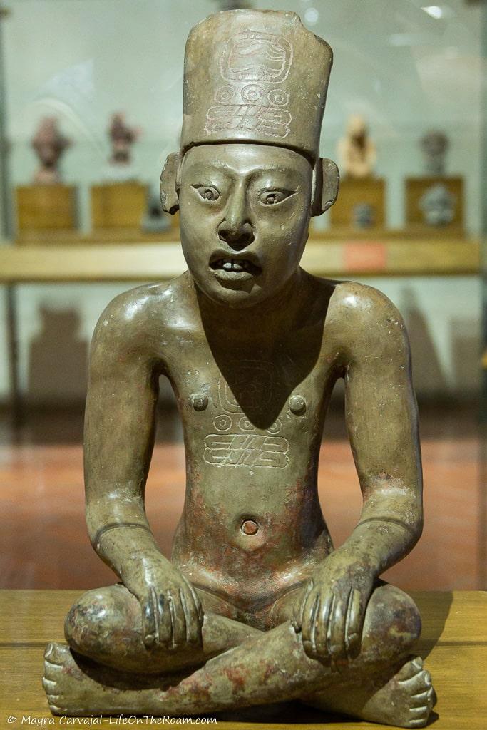 A pre-Columbian figure of a man sitting with his legs crossed