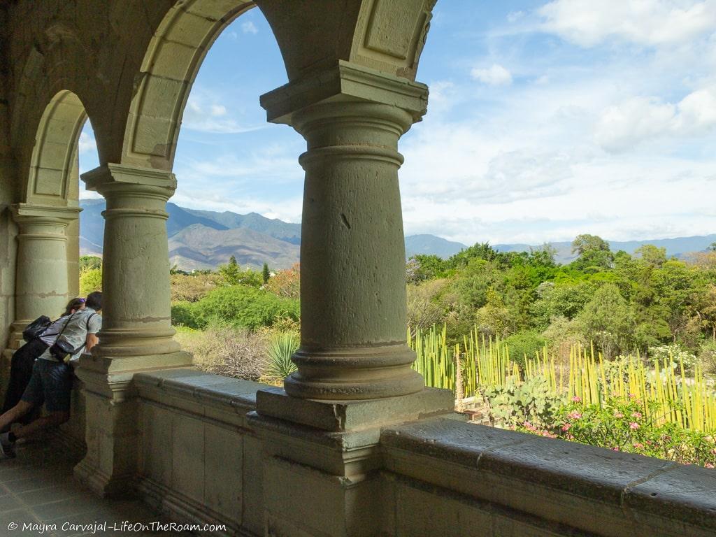 View of a garden and mountains from the arched windows of a corridor