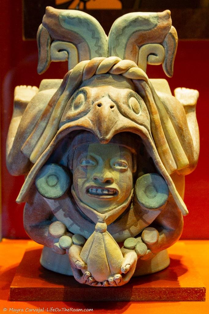 A Mayan sculpture of a man coming out of a bird-like creature while holding a cacao pod