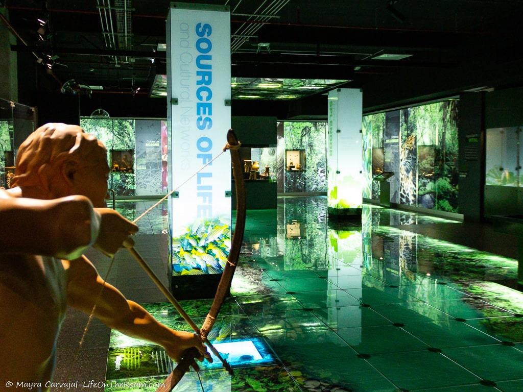 An exhibit hall with illuminated panels and the figure of a man with a bow and arrow