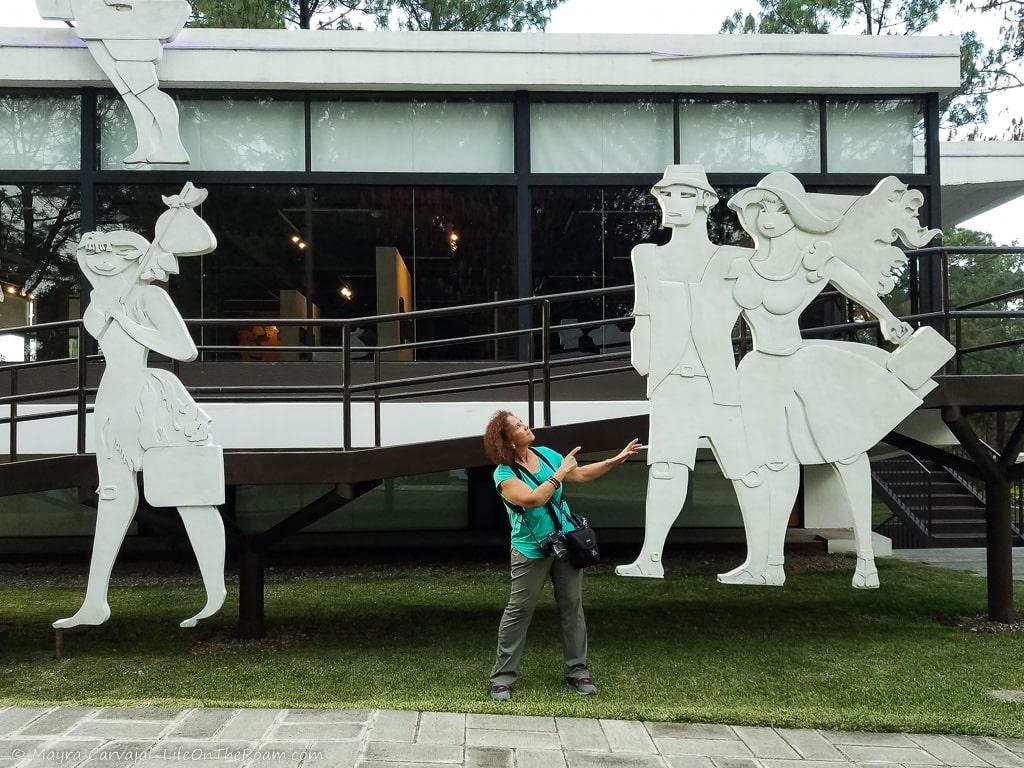 A woman standing next to large human-like sculptures at the entrance of a glass building