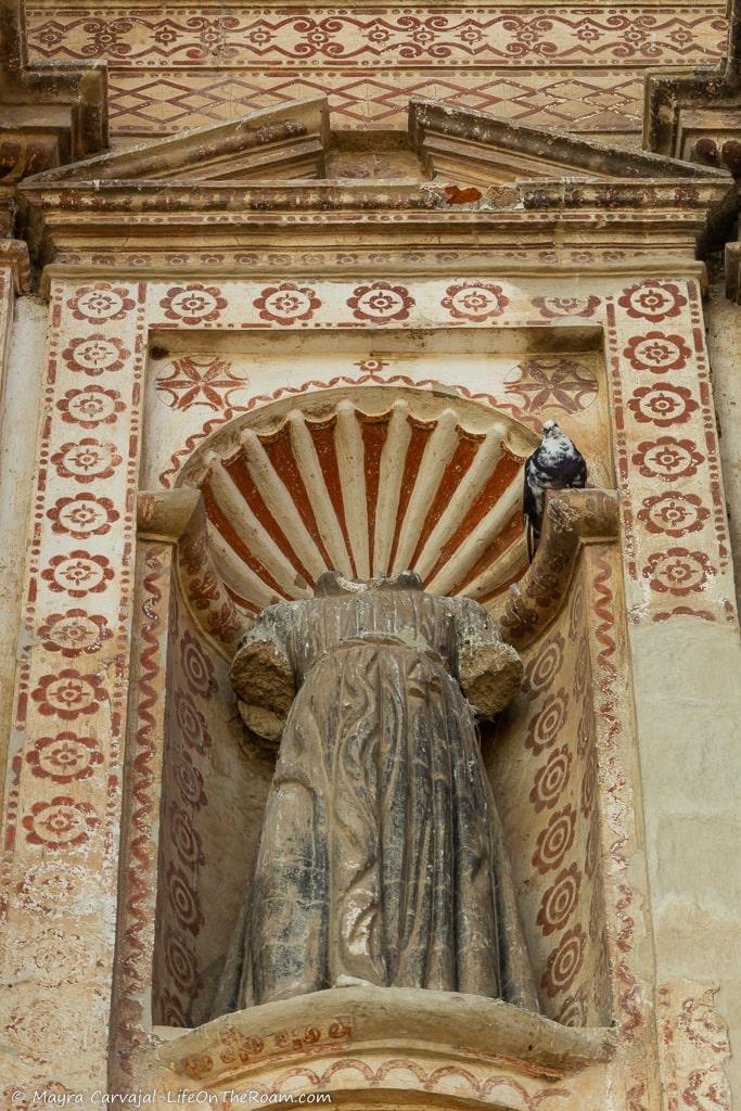 A headless statue in a decorated niche with a shell shape at the top.