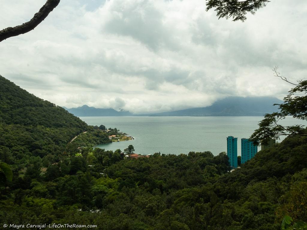View of a lake and cloud-covered volcanoes through the forest