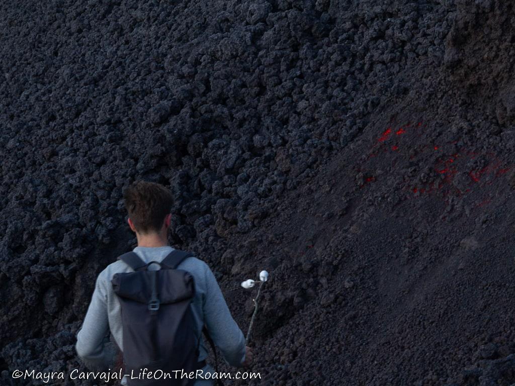 A man roasting marshmallows near volcanic lava