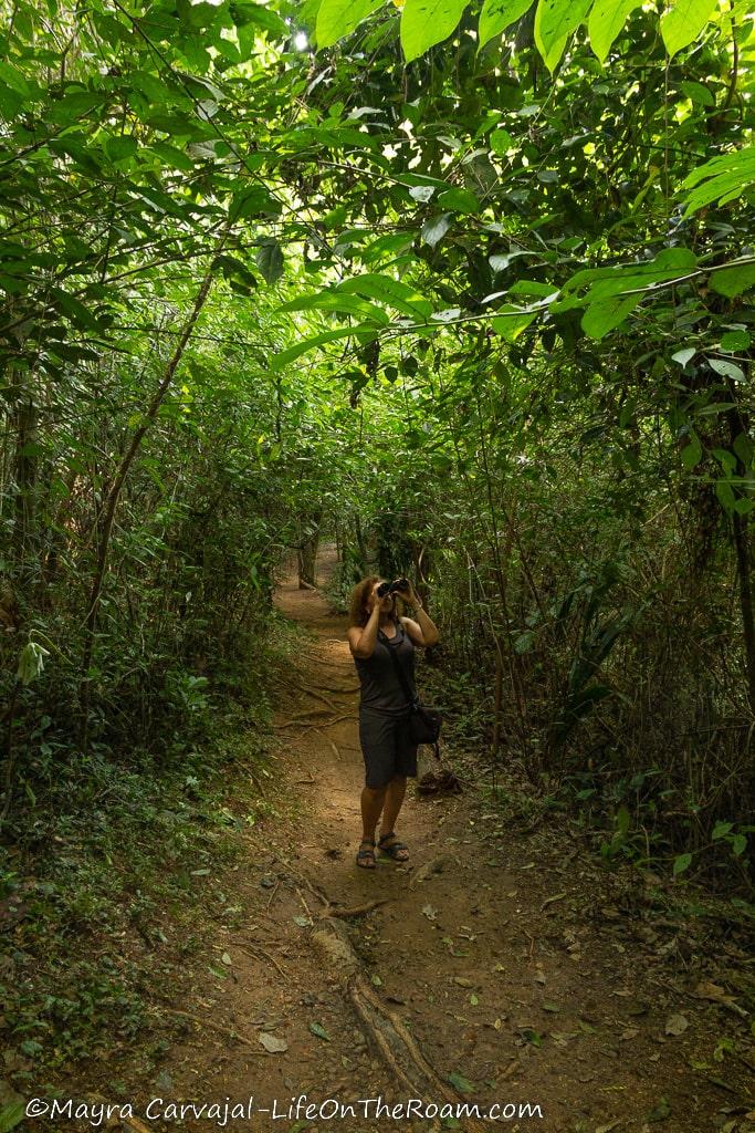 A woman with binoculars in a forest trail