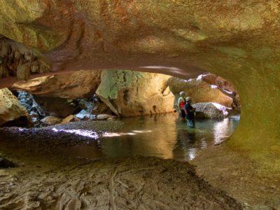 2 men standing inside a big cave with a river