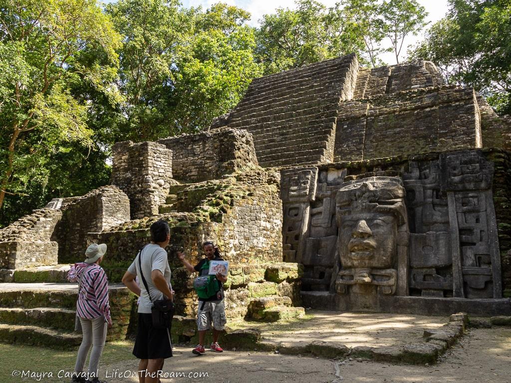 People looking at an ancient temple with a big mask on the right