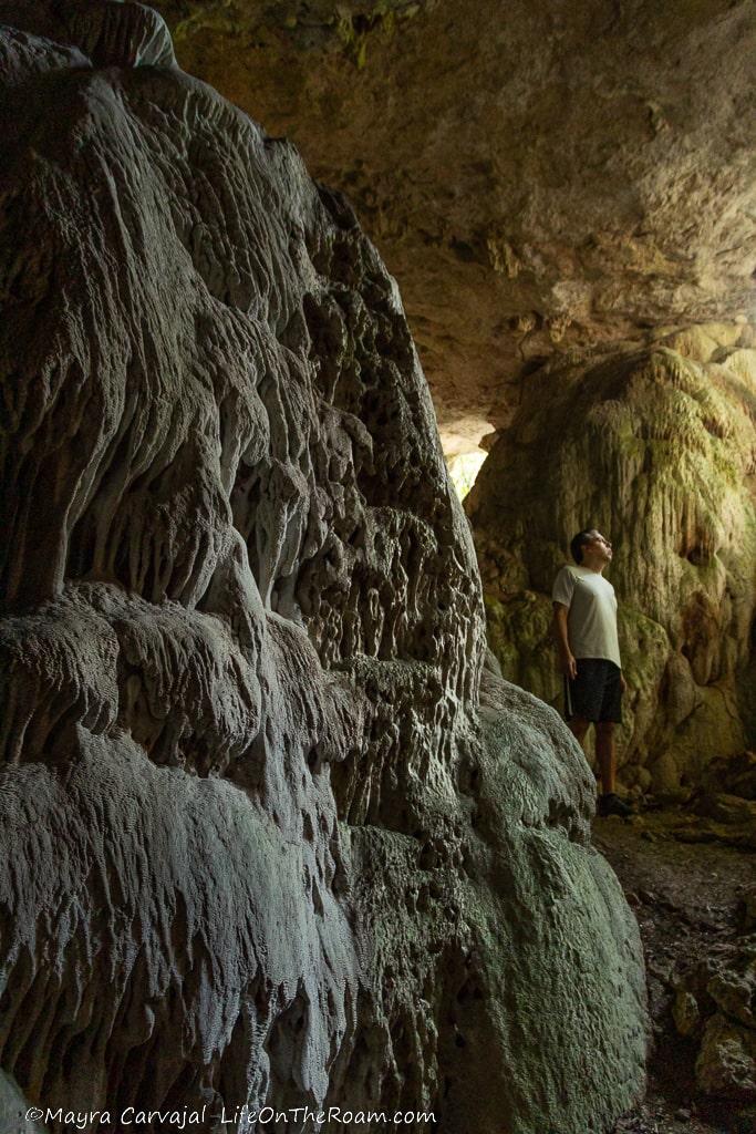 A man standing at the entrance of a cave with calcium carbonate formations in the foreground