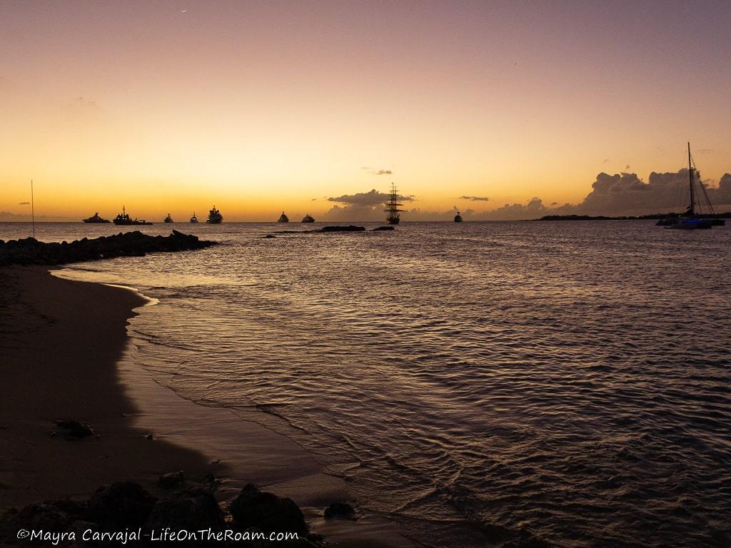 A sunset on a beach with boats in the distance