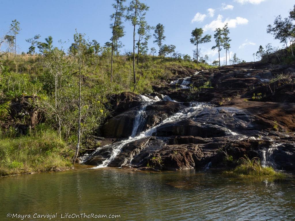 A cascade with water flowing down large boulders into a pond