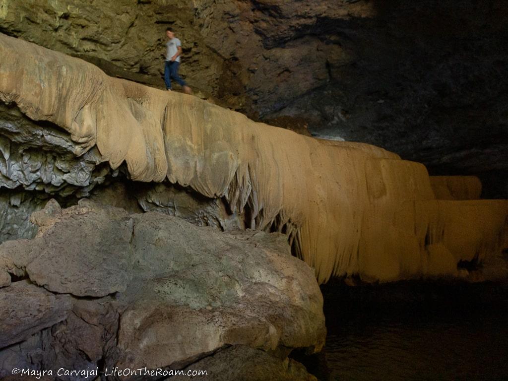 A person walking above a formation inside a tall cave