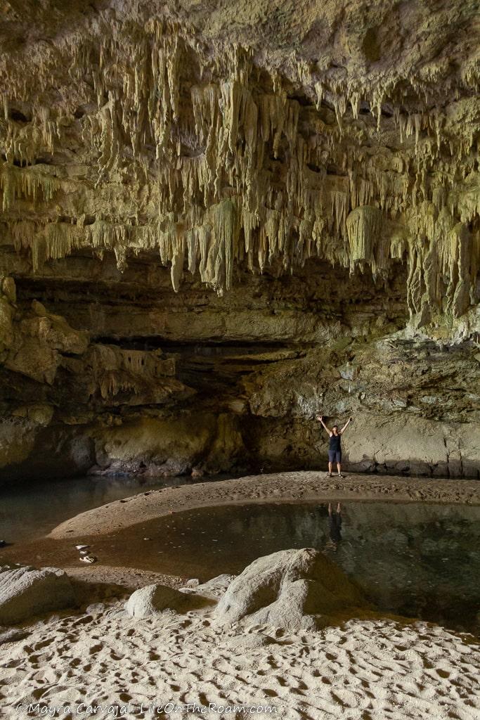 A woman standing at the edge of a pool formed by a river running through a cave with stalactites