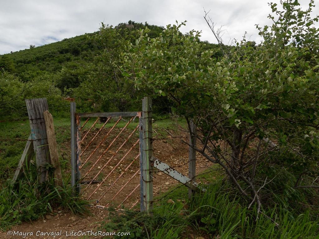A low iron gate at the entrance of a trail with hills in the background