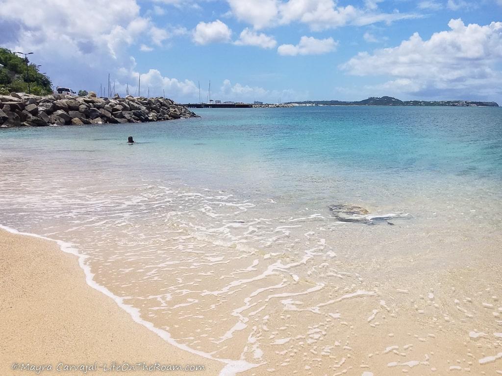 A crystal-clear-water sandy beach with a pier in the background