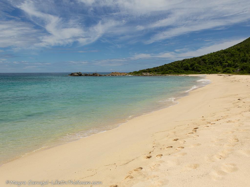 A deserted sandy beach with a verdant hill in the background