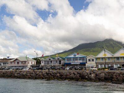 A waterfront with colourful 2-storey traditional buildings with a volcano in the background