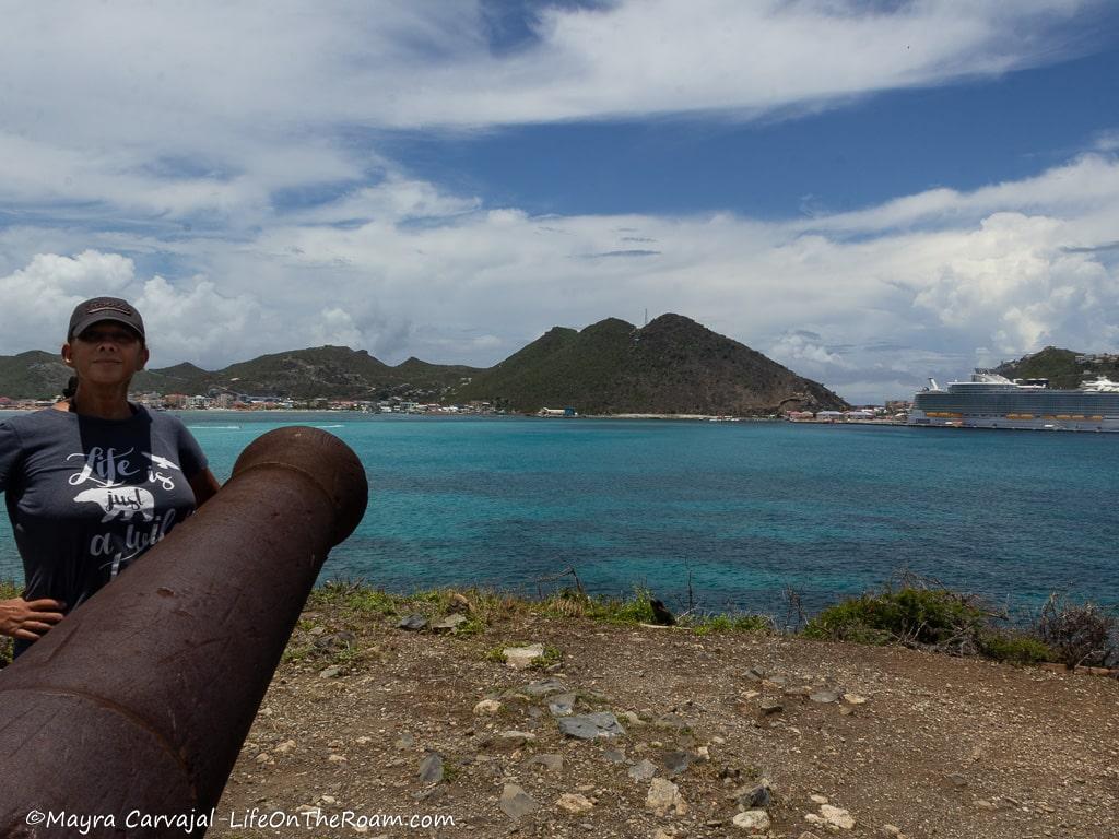 Mayra standing next to a cannon with the sea and hills in the background