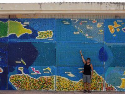 Woman pointing at St Maarten on a colourful mosaic depicting a map of the Caribbean made of bottle caps