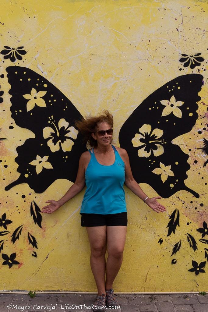 Mayra standing in front of a mural of big butterfly wings