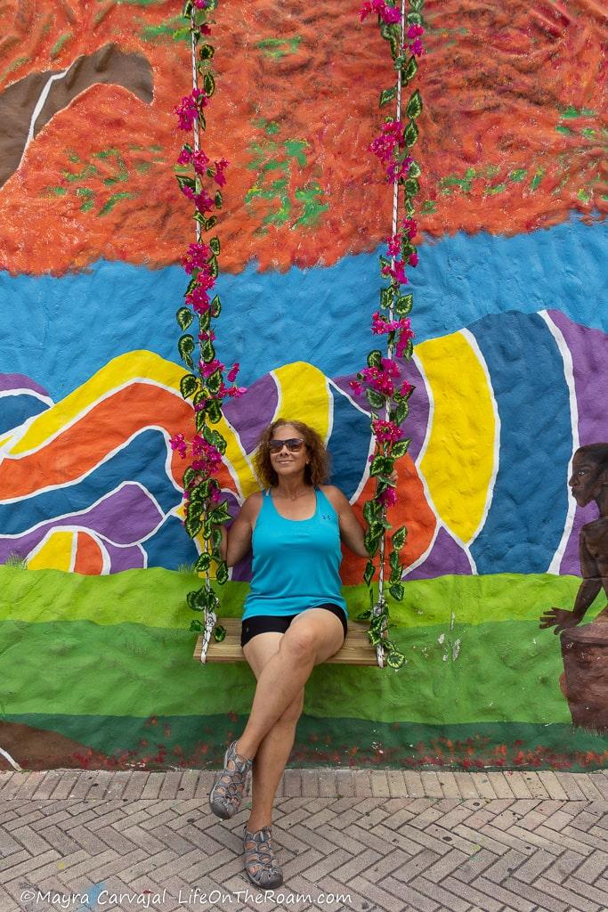 Mayra sitting on a bench that integrates into a colourful mural as a swing