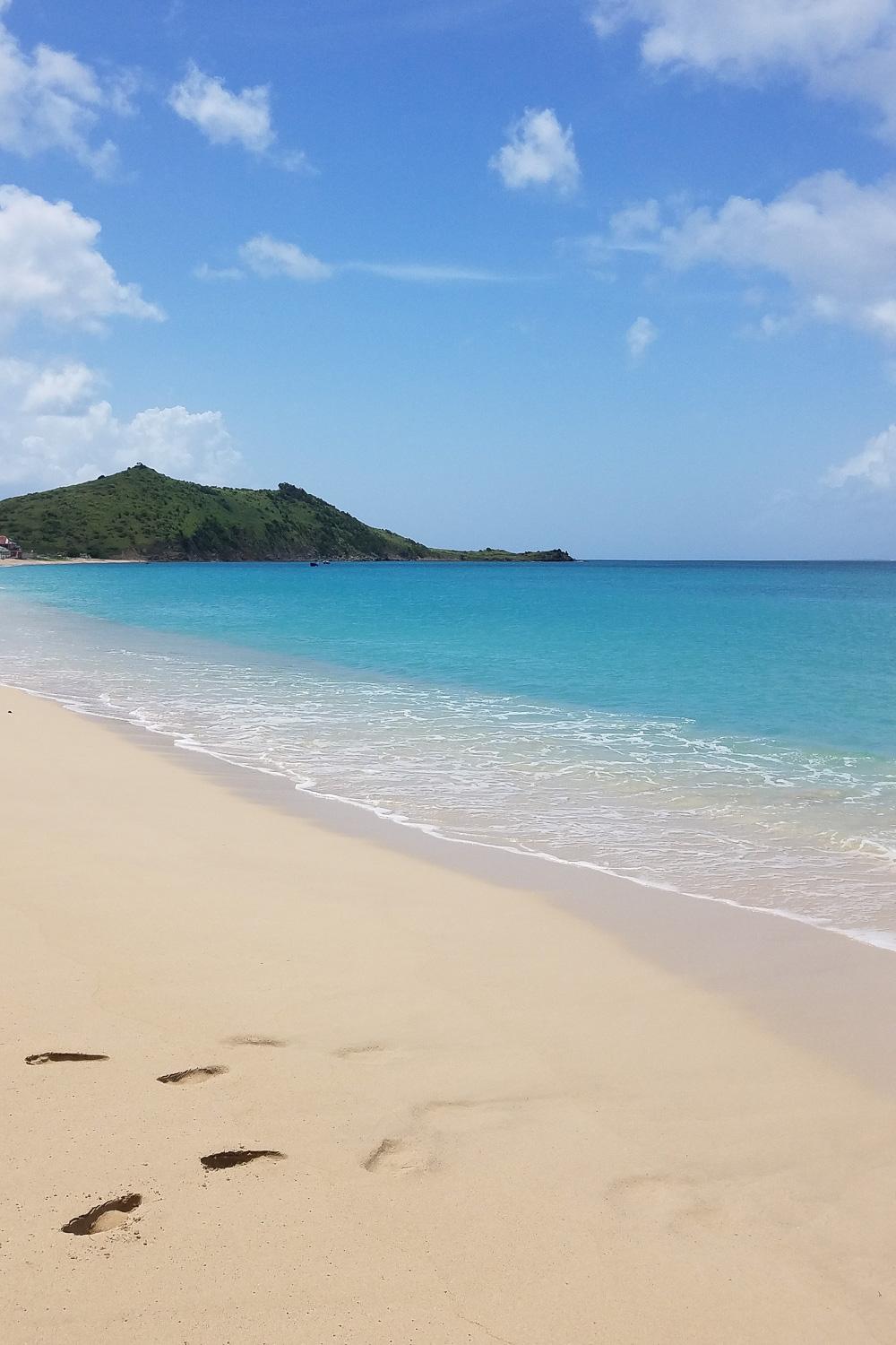 A beach with soft sand, turquoise waters and a hill in the background