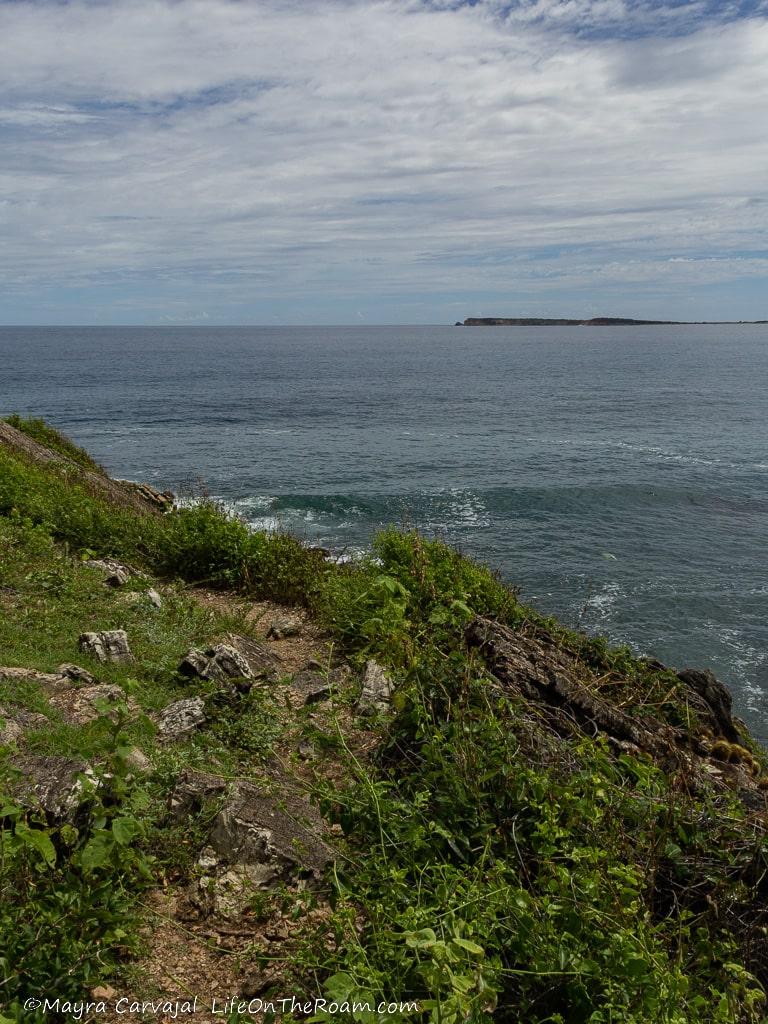 A narrow coastal trail with views of the sea and a distant island