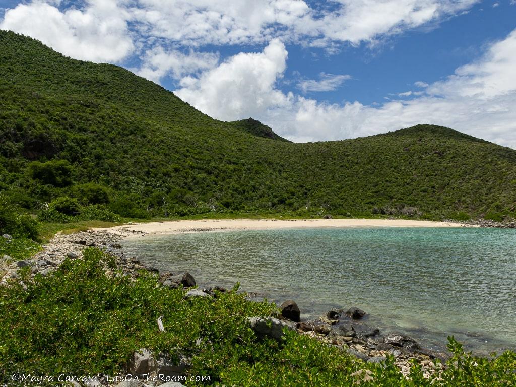 A sandy beach in a bay surrounded by hills covered with a dry forest