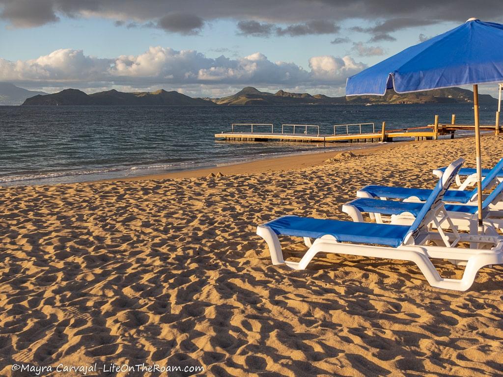 A sandy beach with blue lounge chairs and umbrellas