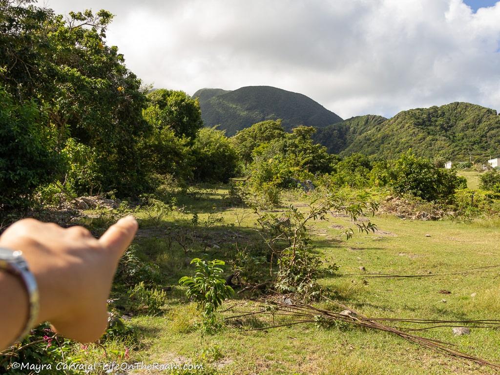 Mayra's hand pointing towards a grassy path with mountains in the background