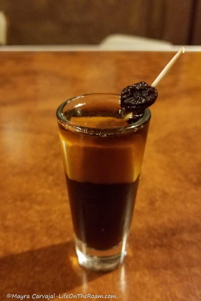 A drink in a shot glass with a piece of cheese inside and a raisin