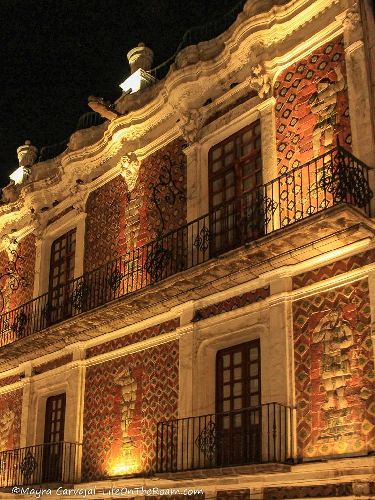 The illuminated façade of a building covered in brick and tiles