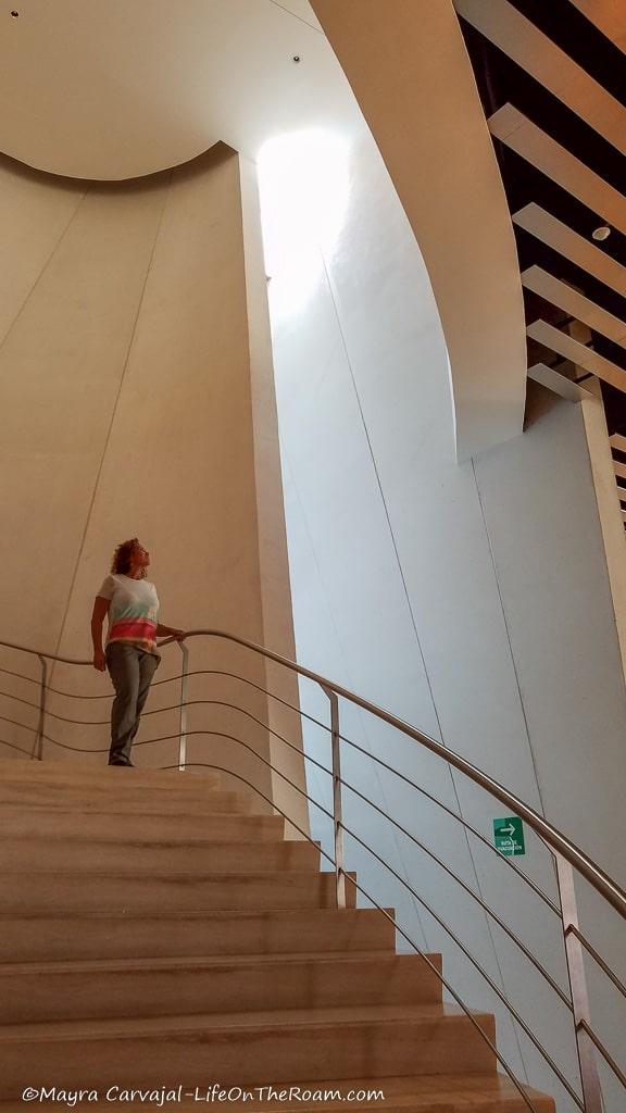 Mayra standing at the top of a curved staircase looking at the curved walls inside the museum
