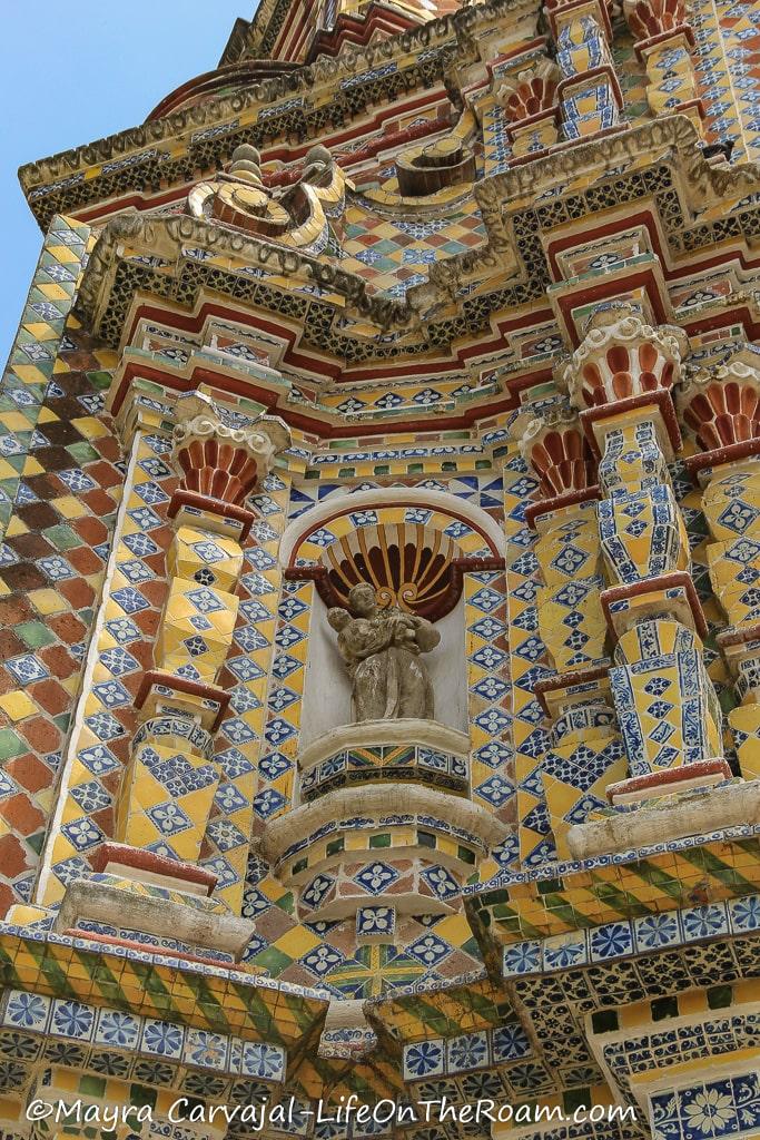 A niche in a facade flanked by columns, covered in multicolour tile