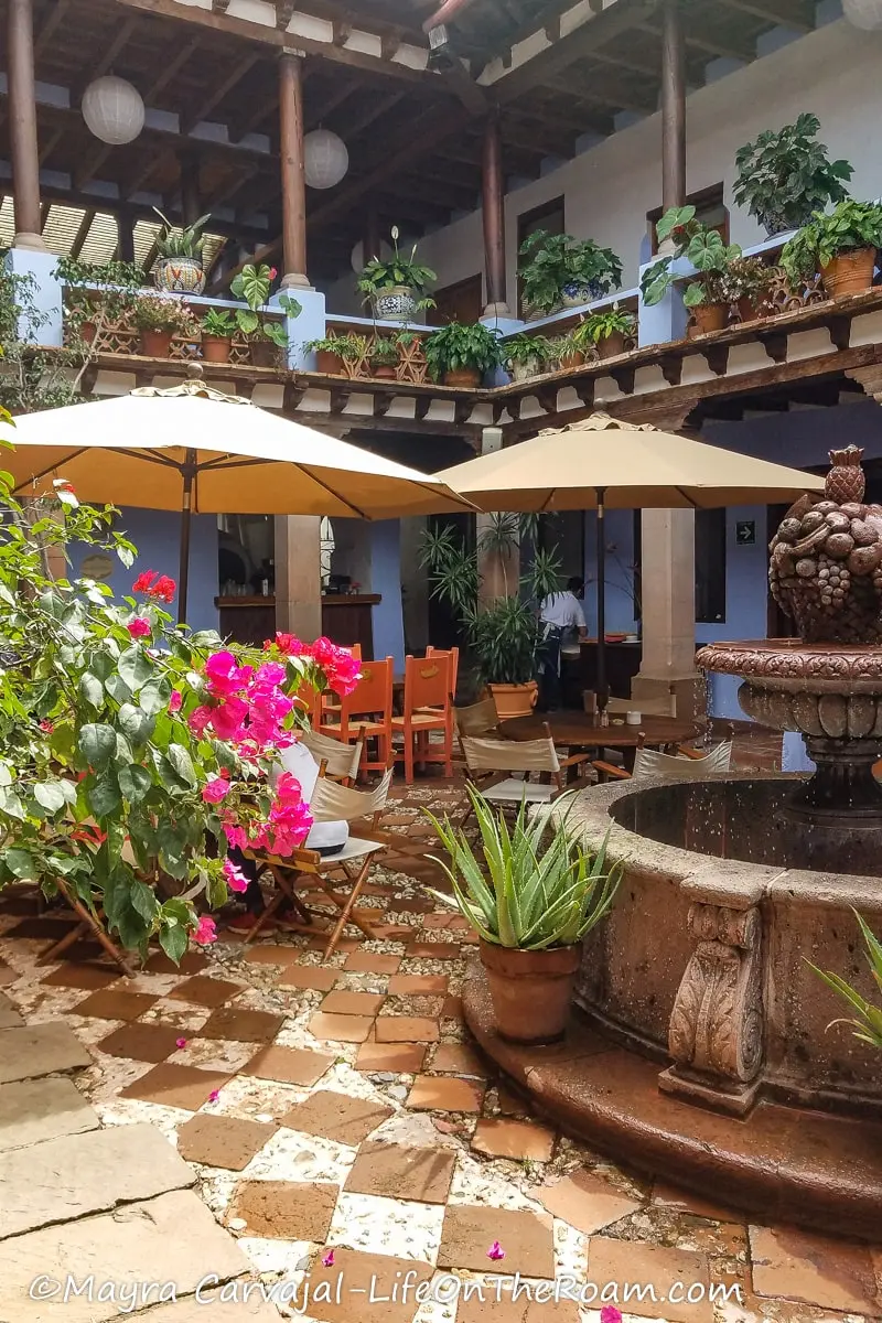 The inner patio of a colonial house with a fountain and tables with umbrellas