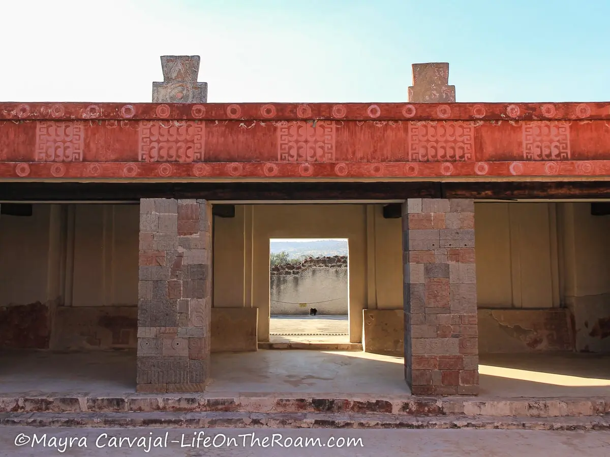 A courtyard with carved columns and a band with red painting