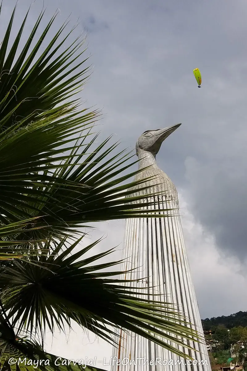 A statue of a bird with someone paragliding above