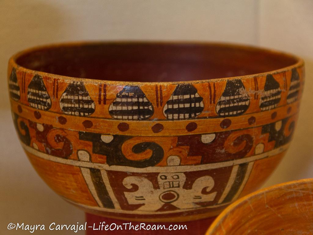 A polychromatic round and short vase with orange and red tones and black drawings