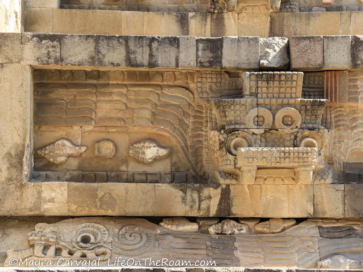 Frieze on an ancient building depicting slithering serpents among shells and serpent wearing headdresses
